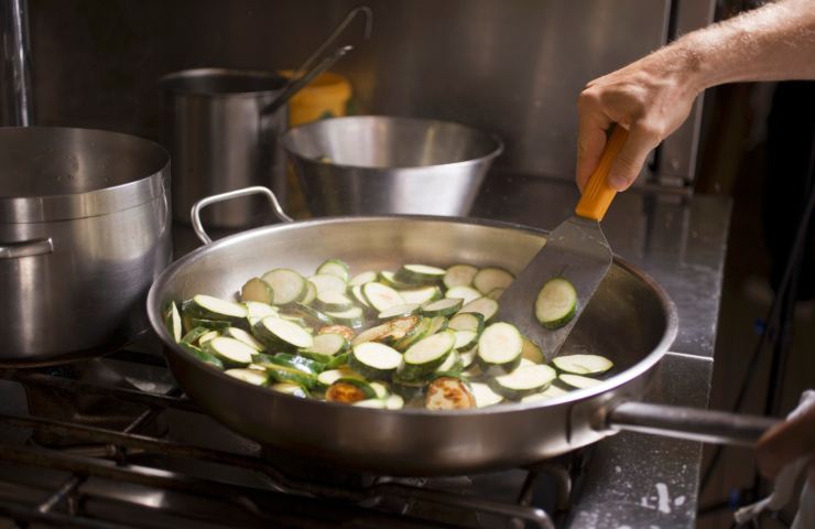 uomo che cucina zucchine in padella