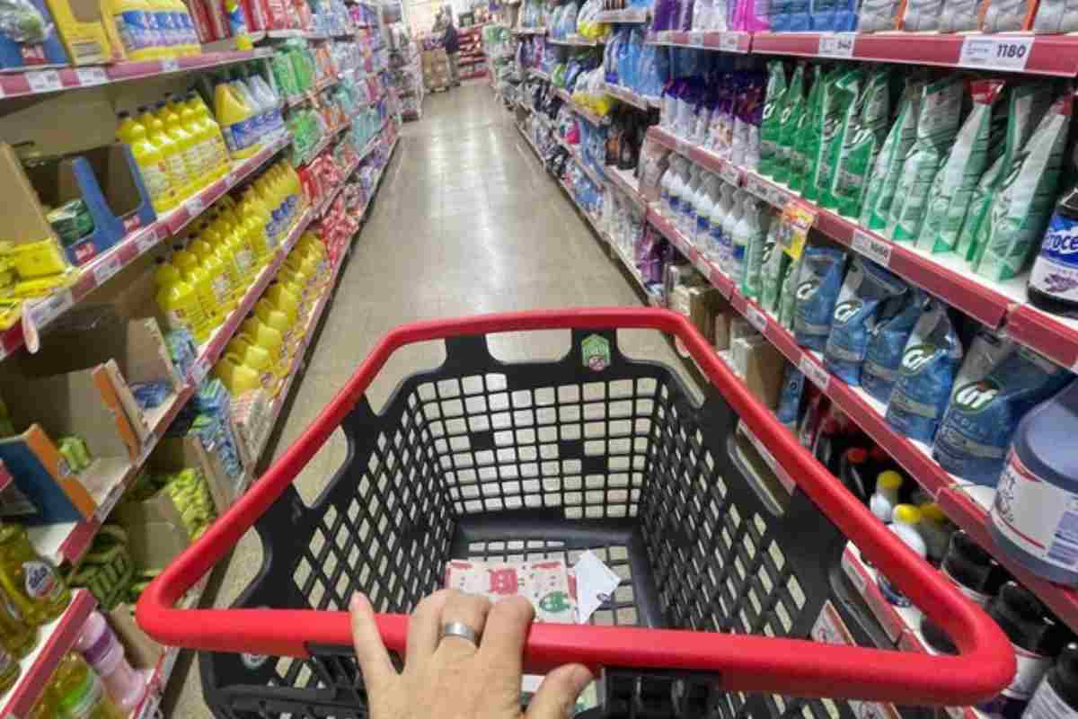 mano che spinge carrello tra le corsie del supermercato