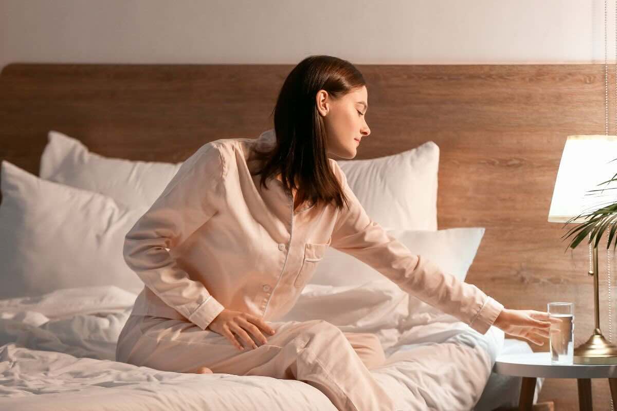 Ragazza in pigiama seduta sul letto, bicchiere sul comodino
