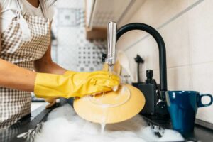 Mano con guanto giallo lava piatto giallo sotto acqua corrente