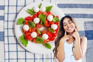 piatto con fresella, pomodorini e mozzarella e donna che simula il gesto buono