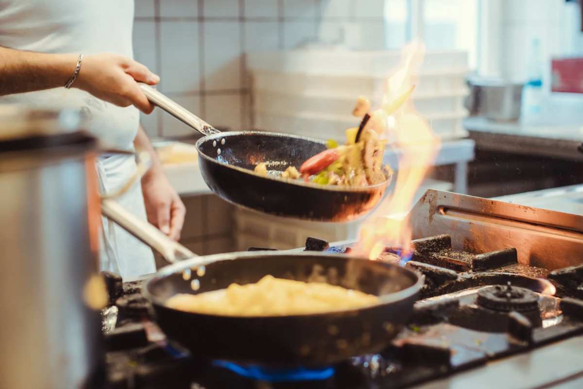 Uomo che cucina con padelle sul fuoco